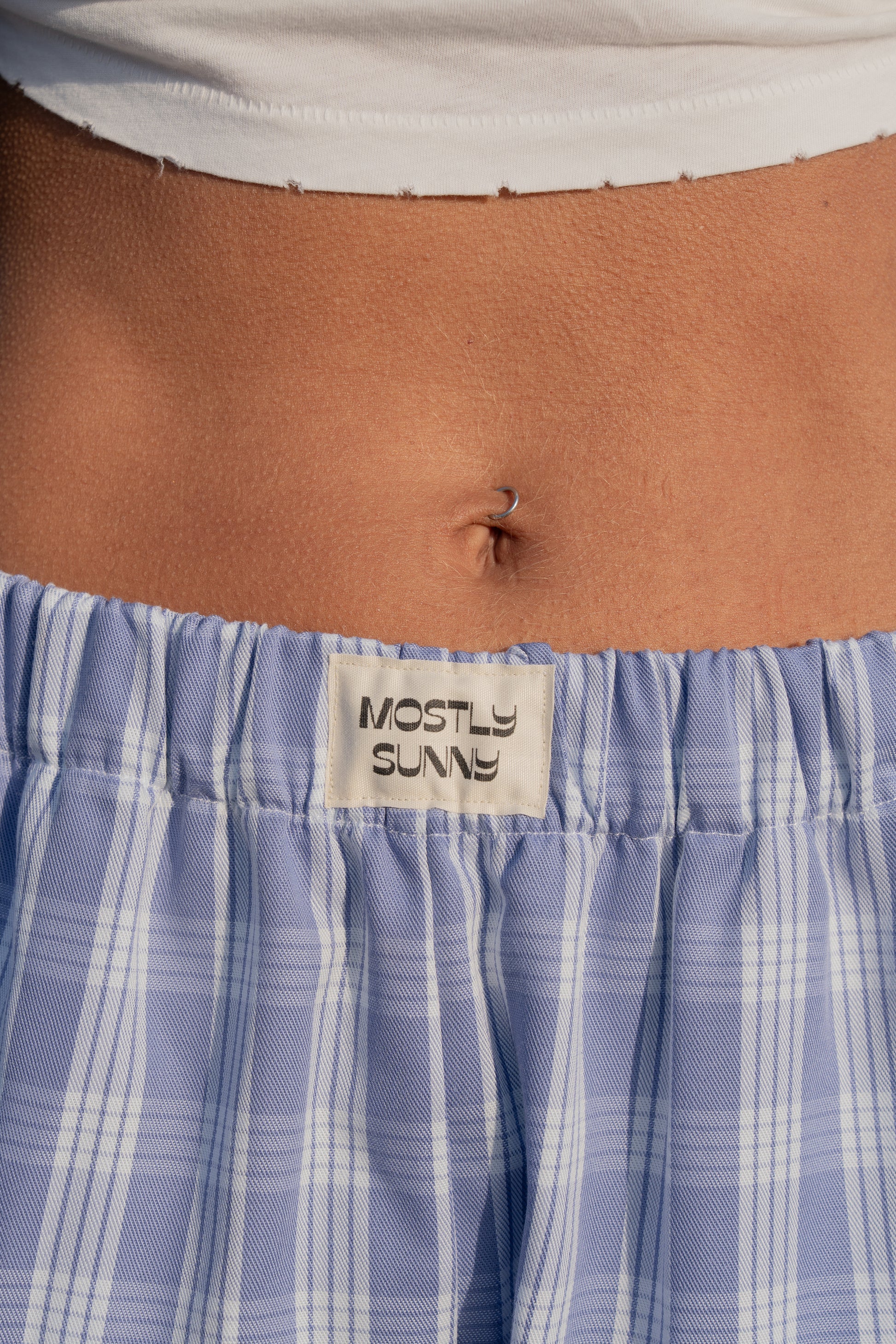 Close-up of a person wearing blue palaka lounge pants with 'Mostly Sunny' label.