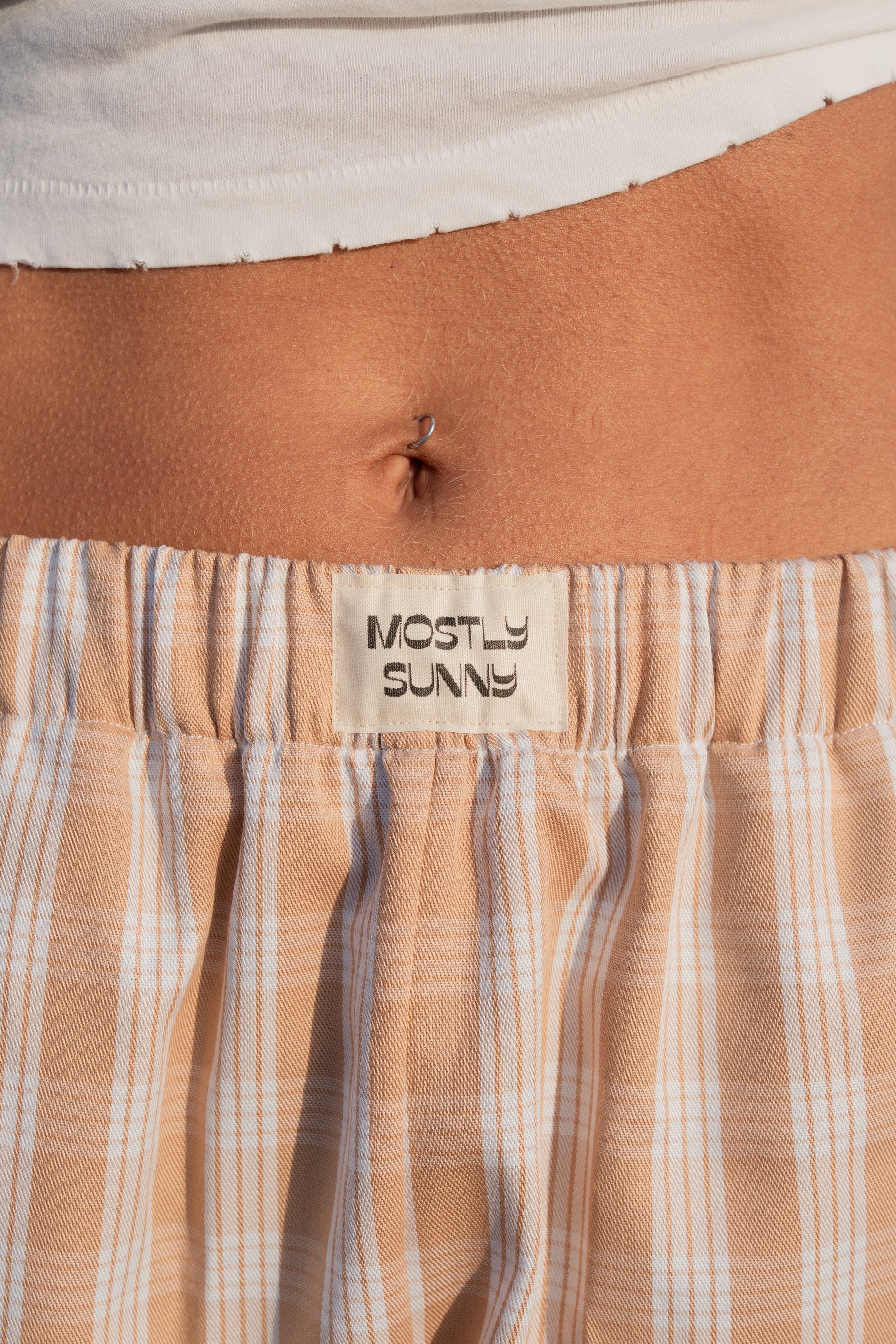 Close-up of palaka sand lounge pants with a 'Mostly Sunny' label.